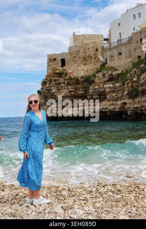 Schöne junge Frau posiert am Mittelmeer mit traditionellen weißen Gebäuden und felsiger Küste im Hintergrund. Stockfoto