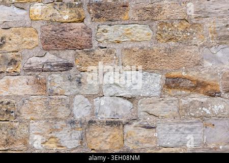 Nahaufnahme der verwitterten Sandsteinmauer mit Mörtelfugen und verschiedenen Steinblöcken aus einem alten historischen Gebäude, geeignet als Architektur oder Co Stockfoto
