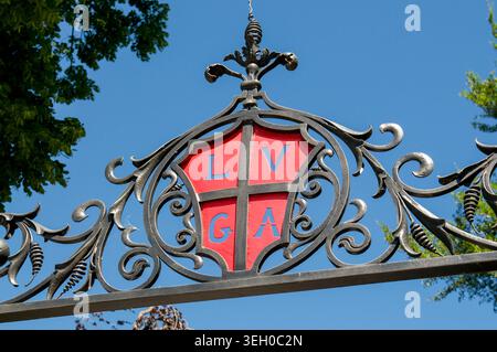 Nahaufnahme des historischen Wappens von Lugano, Schweiz, mit einem roten Schild mit den Buchstaben LVGA in einem kunstvoll verzierten schwarzen schmiedeeisernen Tor. Cle Stockfoto