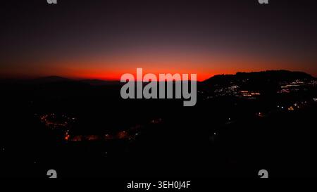 Abendhimmel mit rotem Licht über Silhouettenberge und funkelnden Lichtern der Stadt Stockfoto