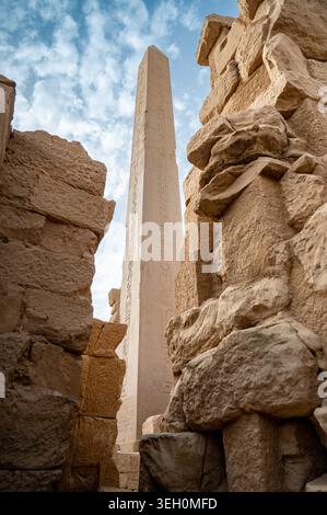 Flacher Blick auf einen hohen alten ägyptischen Obelisken, bedeckt mit Hieroglyphen, der zwischen massiven Sandsteinruinen im Karnak Tempelkomplex in Luxor aufsteigt. Stockfoto