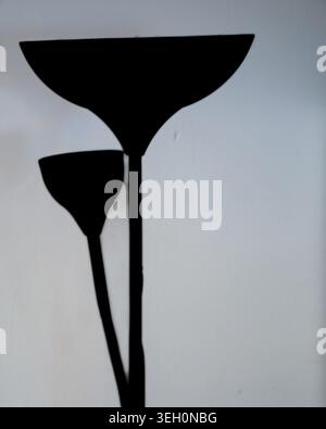 Minimalistisches schwarzes Design der Stehleuchte vor einer hellgrauen Wand mit sanftem Innenlicht, abstrakten Formen und sauberem Kopierraum. Stockfoto