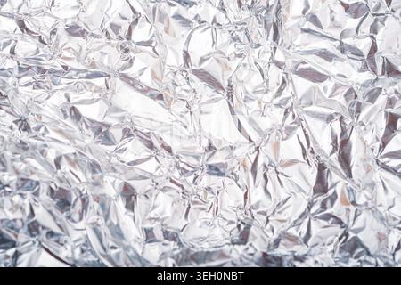 Glänzende, zerknitterte Aluminiumfolie mit reflektierenden Silberfalten, scharfen Highlights und abstraktem Metallic-Muster für Designhintergründe. Stockfoto