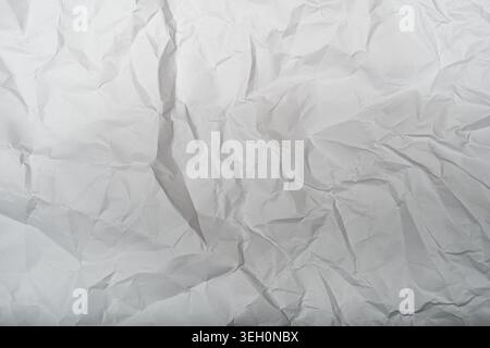 Nahaufnahme von weißem zerknittertem Papier mit tiefen Falten, dezenten grauen Schatten und ungleichmäßigen Falten für abstrakte Textur oder Hintergrund. Stockfoto