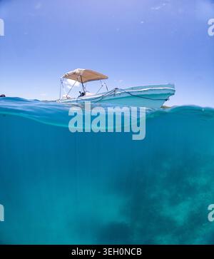 Blick auf ein kleines Boot, das auf dem türkisfarbenen karibischen Meer mit klarem blauen Himmel in Guanaja, Bay Islands Department, Honduras schwimmt. Stockfoto