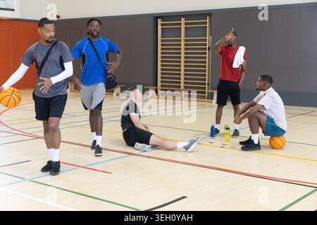 Verschiedene männliche Teamkollegen in Sportbekleidung dribbeln, sitzen und ruhen sich mit Basketbälle auf dem Fitnessplatz aus Stockfoto