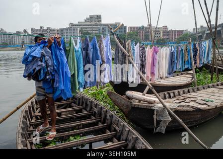 Dhaka Division, Bangladesch - 14. Mai 2026: Blick auf einen Mann, der seine Wäsche an einer Linie über traditionelle Holzboote auf dem Buriganga River mit der Stadt hängt Stockfoto