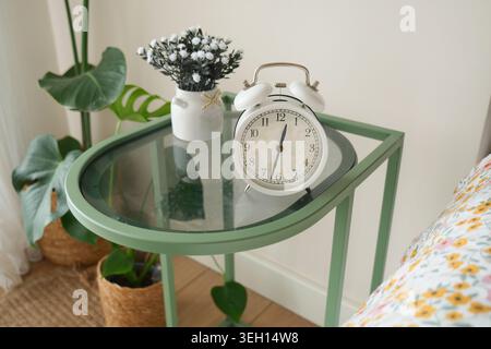 Uhr und Blumen auf einem Nachttisch im Zimmer Stockfoto