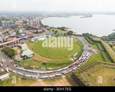 Blick aus der Vogelperspektive auf das Galle International Stadium und die historischen Festungsmauern mit Bussen, die entlang der Straße und der Bucht in der Ferne Galle, Southern PR Stockfoto