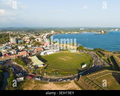 Aus der Vogelperspektive auf das Galle International Stadium und die historischen Festungsmauern entlang der Küste unter klarem Himmel in Galle, Südprovinz, Sri Lanka. Stockfoto