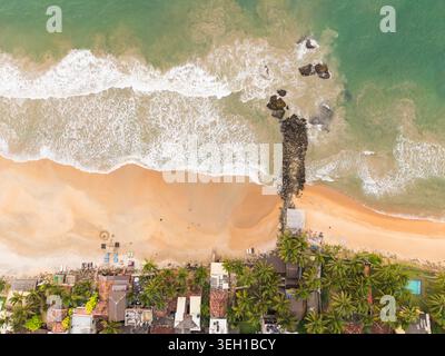 Aus der Vogelperspektive auf einen Sandstrand mit stürzenden Wellen, einem Steinbruch und üppigen Palmen am Ufer in Galle, Südprovinz, Sri Lanka. Stockfoto