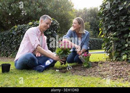 Ältere Frau und Tochter Pflanzen rosa Topfblumen im Garten mit Kelle und Kindergarten Topf Stockfoto