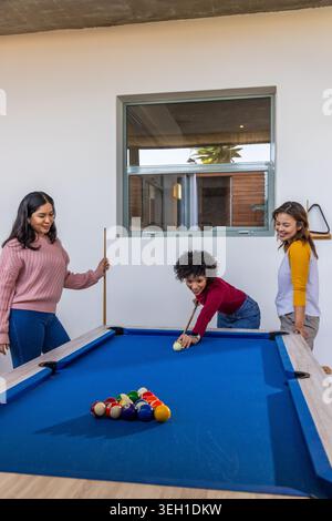 Verschiedene weibliche Freunde, die auf blauem Billardtisch im Spielzimmer mit Kugeln und Hinweisen schießen Stockfoto