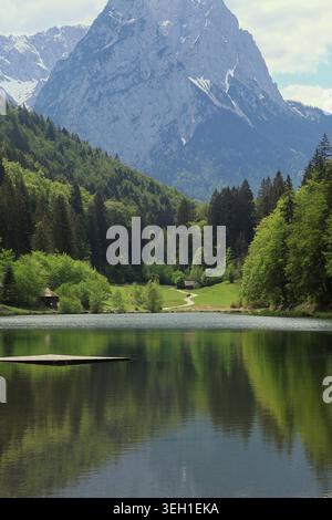Die schneebedeckten Bayerischen Alpen, eingebettet zwischen grünen Wäldern und einem See mit Wanderweg, im Frühjahr Stockfoto
