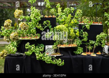 Ein wunderschön dekorierter Buffettisch bietet professionelle Catering-Snacks an Ständen inmitten üppig grüner Hortensien Stockfoto