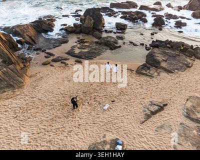 Aus der Vogelperspektive eines Paares, das während der goldenen Stunde in Galle, Südprovinz, Sri Lank an einem Sandstrand spaziert, umgeben von großen Felsen und stürzenden Wellen Stockfoto