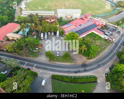 Aus der Vogelperspektive auf einen Gebäudekomplex mit Solarpaneelen und einen Parkplatz neben einer gekrümmten Straße und das Galle International Stadium in Galle, Southern Pro Stockfoto