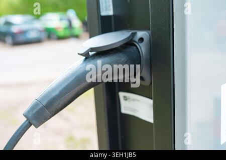 Anschluss für das Ladegerät für Elektrofahrzeuge mit verschwommenem Parkplatzhintergrund. Grüne Technologie, saubere erneuerbare Energien, Lebensstil der Zukunft, Makroansicht. Stockfoto
