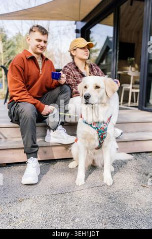 Eine entspannte Frau und ein Mann verbrachten einen ruhigen Morgen mit einem Hund in der Nähe eines kleinen Hausrefugiums Stockfoto