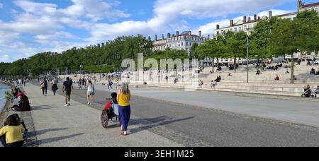 An einem sonnigen Tag entspannen sich die Menschen und fahren mit dem Fahrrad entlang einer modernen Uferpromenade mit Steintreppen in Lyon, Frankreich. Stockfoto