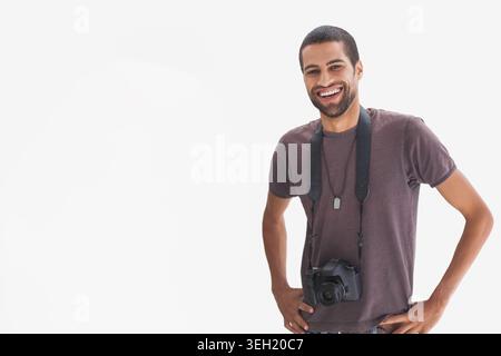 Mittelgroßer Mann, der im Studio Hände auf Hüften posiert, kastanienbraunes T-Shirt trägt, DSLR-Aufhängung, Kopierraum Stockfoto