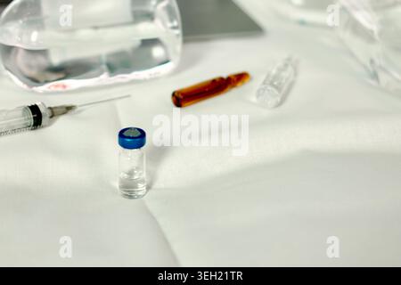 Minimale medizinische Zusammensetzung mit Impfstofffläschchen, Spritze und medizinischen Werkzeugen auf weißem Stoffhintergrund. Berufskonzept für die Impfung Stockfoto