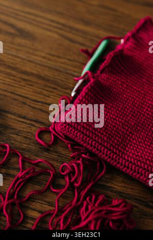 Nahaufnahme von rotem Garn und Häkelprojekt mit Häkelnadel auf dem Tisch Stockfoto