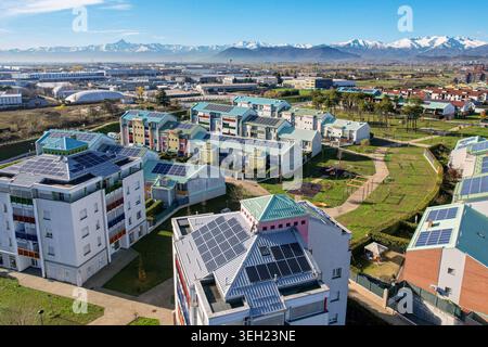 Aus der Vogelperspektive auf modernen Wohngebäuden mit Solarpaneelen auf Dächern und Grünparks mit den schneebedeckten Alpen im Hintergrund Grugliasco, Red Stockfoto