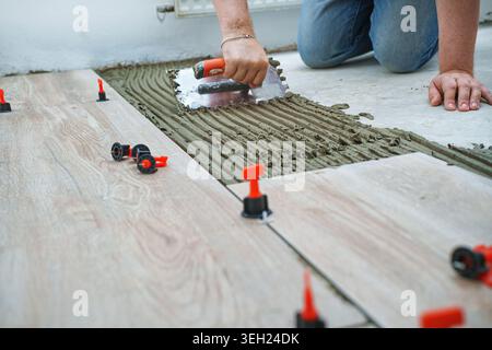 Das Konzept der Verlegung von Fliesen. Fliesen, Spachtel und Leim beim Verlegen von Fliesen mit Nahhänden. Ziehen Sie Laschen und Keile zum Nivellieren des Systems. Stockfoto
