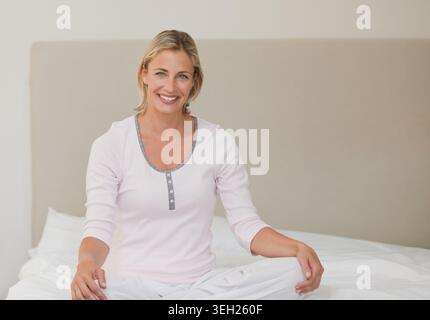 Frau mittleren Alters, die im Querschnitt im Bett im Schlafzimmer saß und einen pinkfarbenen Pyjama neben dem beigefarbenen Kopfteil trug Stockfoto