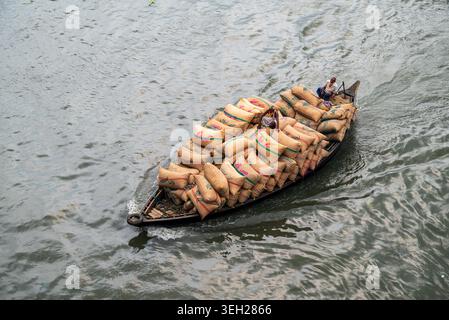 Dhaka Division, Bangladesch - 14. Mai 2026: Aus der Vogelperspektive eines mit Jute-Säcken beladenen Holzbootes und zweier Männer, die den Buriganga River befahren. Stockfoto