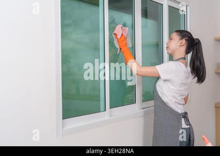 Asiatische Frau putzt Fenster mit Tuch im modernen Zuhause Stockfoto