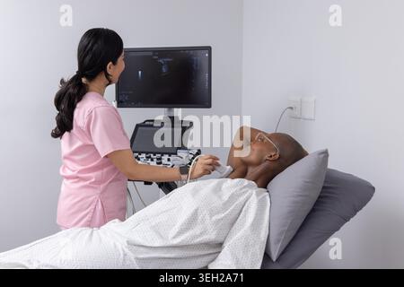 Verschiedene Klinikerinnen in Peelings, Patienten, die auf dem Untersuchungsbett liegen und Ultraschall mit Schallkopf und Bildschirm erhalten. Sonographie, Monitor, Sonograf, Kabel, Klinik, Gesundheitswesen, Geräte Stockfoto