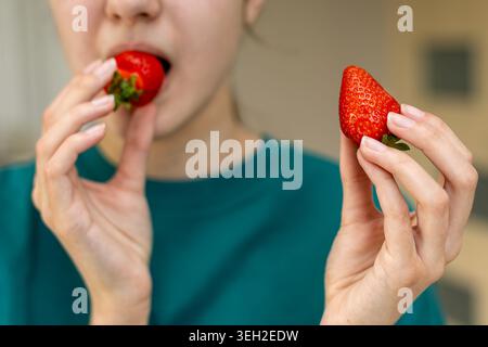 Frau isst frische Erdbeeren aus der Nähe. Nahaufnahme einer Frau, die zwei reife rote Erdbeeren hält und eine in den Mund bringt, während die andere bleibt Stockfoto