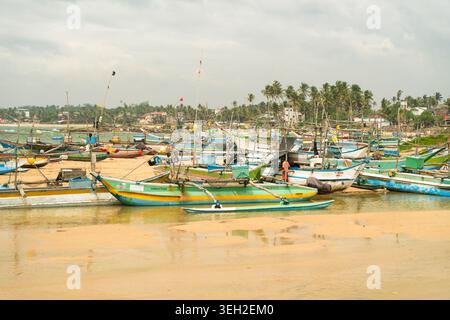 Blick auf traditionelle farbenfrohe Auslegerboote, die am Sandstrand unter einem bewölkten Himmel in Dodanduwa, Südprovinz, Sri Lanka vor Anker liegen. Stockfoto