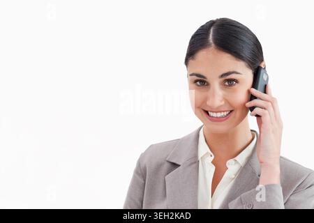 Geschäftsfrau hält schwarzes Telefon am rechten Ohr, lächelt im Studio mit Blazer, Kopierraum Stockfoto