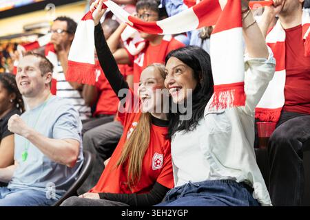Die Fußballfans von Mutter und Teenager lächeln und schwenken während eines Live-Fußballspiels auf überfüllten Stadiontribünen zusammen mit rotem Schal. Intensives Fußballspiel mit leidenschaftlichen Fans. Stockfoto