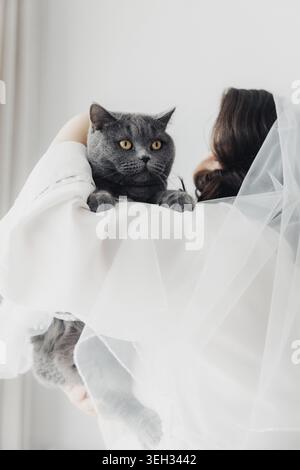 Die Braut hält eine graue Katze, die beide heiter aussieht Stockfoto