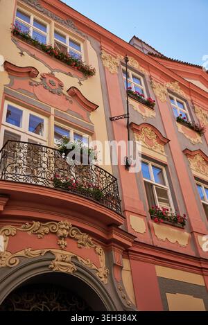 Flacher Blick auf die prunkvolle, pastellrosa und cremefarbene Barockfassade mit bogenförmigem Eingang, schmiedeeisernem Balkon, Blumenkästen und blauen Fenstern Stockfoto