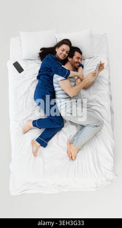 Ein Paar und eine Tochter lachen zusammen auf einem weißen Bett während einer verspielten Morgenroutine Stockfoto