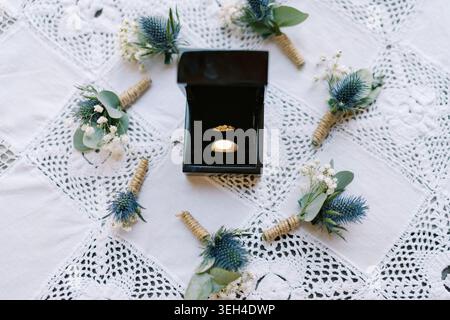Hochzeitsringe in Box mit Boutonniere auf Spitzentischdecke Stockfoto
