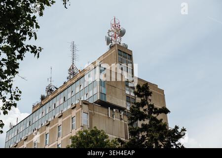 Bürogebäude mit Kommunikationsantennen und Telekommunikationsgeräten unter bewölktem Himmel. Konzept von Rundfunk, Technologie, Infrastruktur und Urbanität Stockfoto