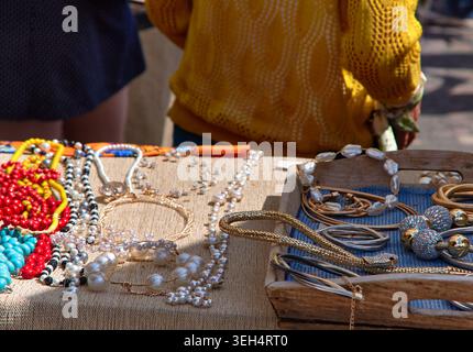 Auf einem Flohmarkt wird eine Vielzahl von handgefertigten Schmuckstücken auf einem Tisch arrangiert, die Halsketten und Armbänder in leuchtenden Farben und einzigartigen Designs präsentieren Stockfoto