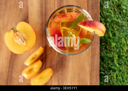 Flaches Lagen eines erfrischenden Glases Pfirsicheistee gefüllt mit Fruchtscheiben und frischen Minzblättern auf hölzernem Hintergrund Stockfoto