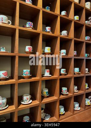 Keramik-Teetassen mit bunten handgemalten Mustern, ordentlich organisiert auf einem modernen quadratischen Holzgitter-Regal für Wohnkultur Stockfoto