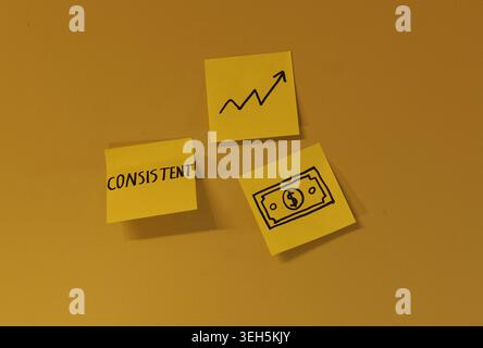 Drei gelbe Haftnotizen, die das Wort „konsistent“ anzeigen, ein aufsteigendes Pfeildiagramm und ein Dollarsymbol, das die Bedeutung von stetigem Bemühen darstellt Stockfoto