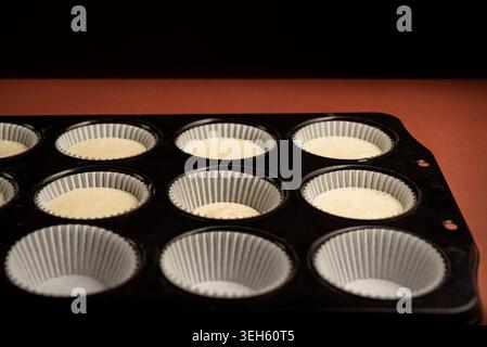 Cupcake-Teig in Papiereinlagen, die vor dem Backen in einem Blech angeordnet sind Stockfoto