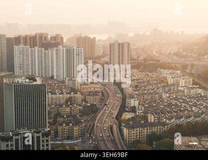 Aus der Vogelperspektive sehen Sie die erhöhte Schnellstraße, die mit Autos besetzt ist, die eine riesige asiatische Metropole unter einem warmen, trüben Morgenhimmel durchqueren Stockfoto