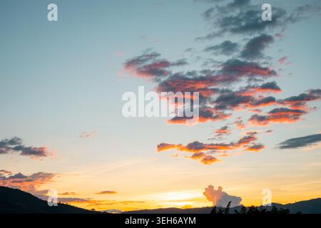 Golden Hour Sonnenuntergang zeichnet Wolken in Orange und Pink über fernen Berglandschaften und schafft so eine ruhige, farbenfrohe Dämmerungslandschaft, die perfekt für den Rücken ist Stockfoto