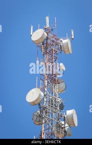 Flachwinkelansicht eines Telekommunikationsturms mit mehreren Mobilfunkantennen und Schüsseln, die auf einer Stahlgitterstruktur gegen eine klare blende montiert sind Stockfoto